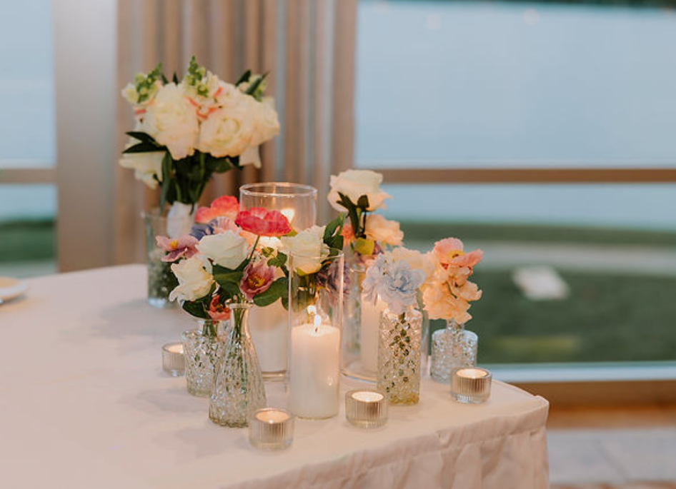 Elegant wedding reception centerpiece featuring blush and coral carnations in crystal vases with pillar candles, styled by Canberra wedding florist and designer.